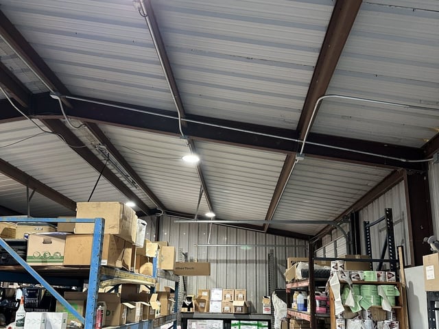 Round LED high-bay fixtures and EMT conduit run along the warehouse roof framing